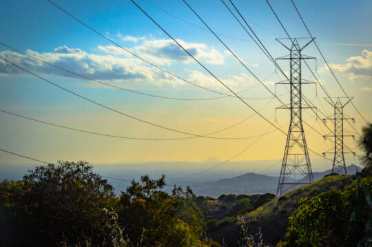 two transmission towers seen looming over greenery with a city visible in the distance