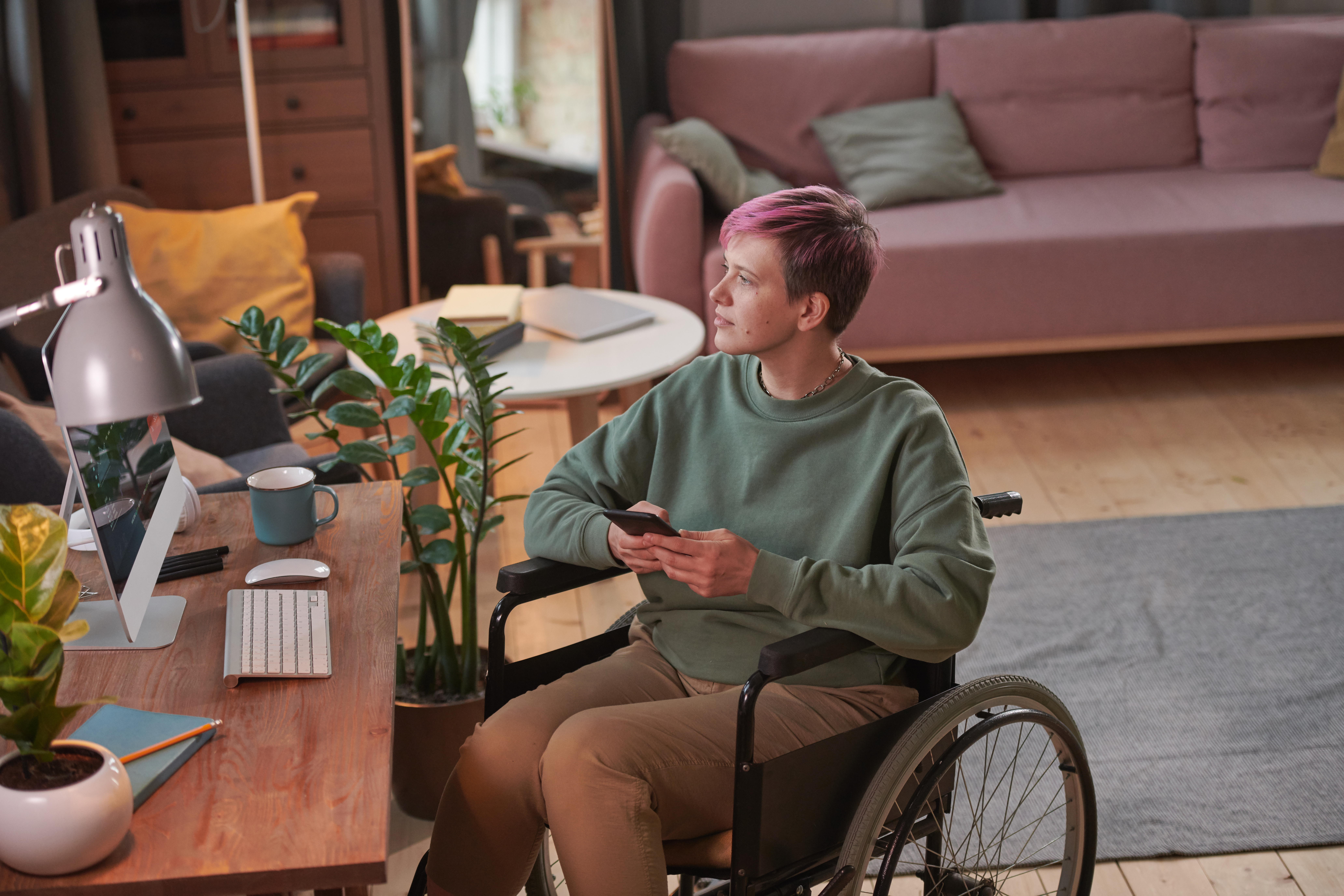 Young woman with short hair sitting in wheelchair in front of her workplace and using her mobile phone