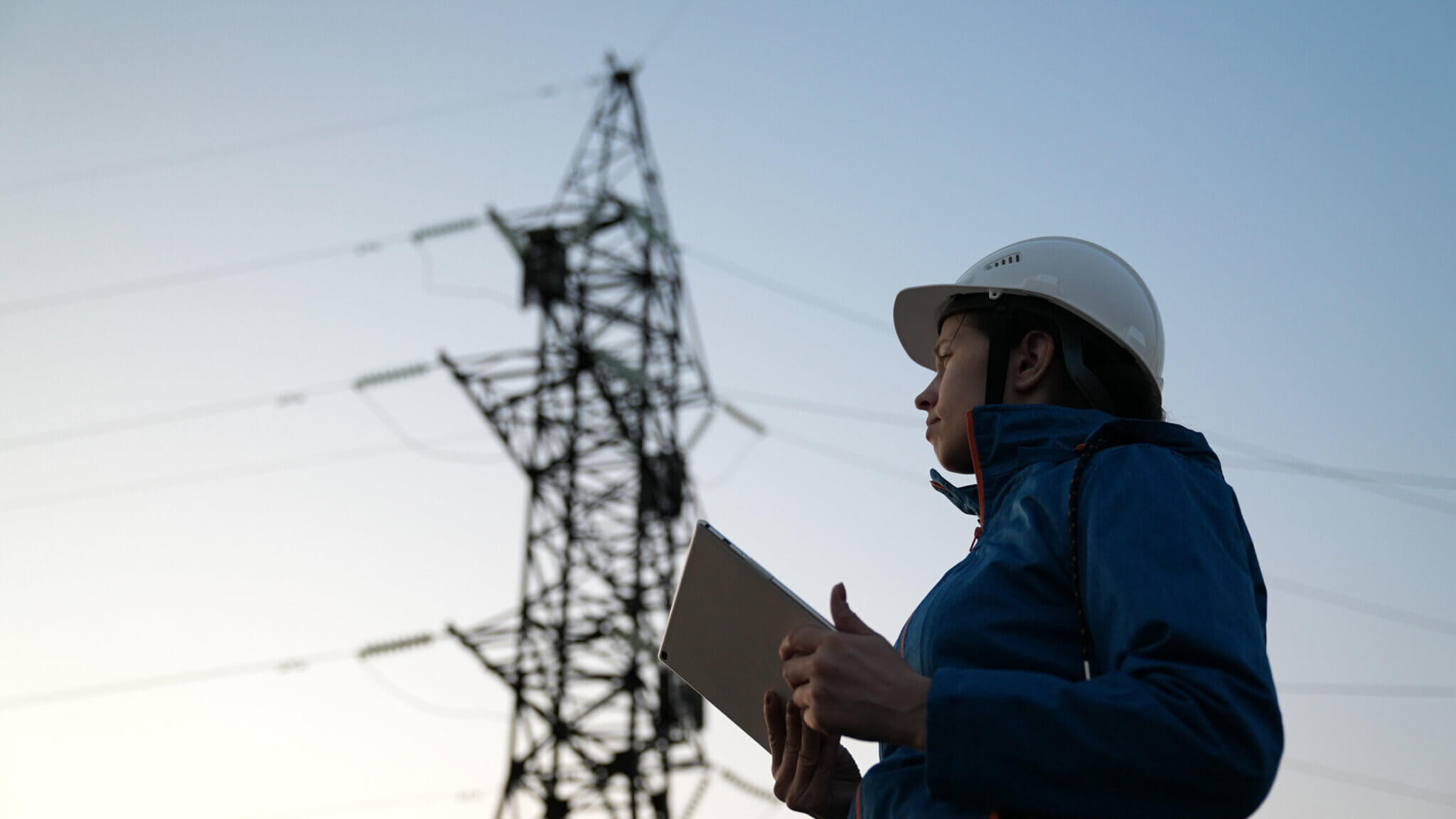 A clean energy technician on the job with a transmission tower in the background.