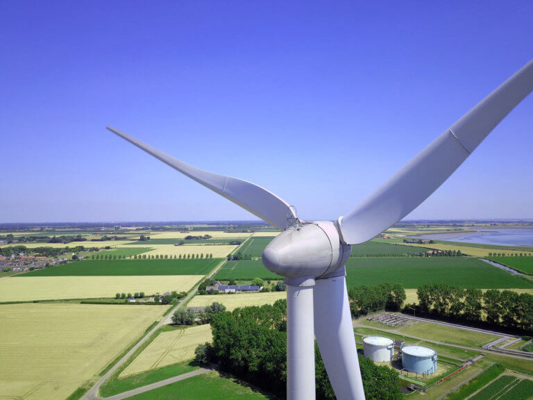 A white wind turbine towering over agricultural fields.