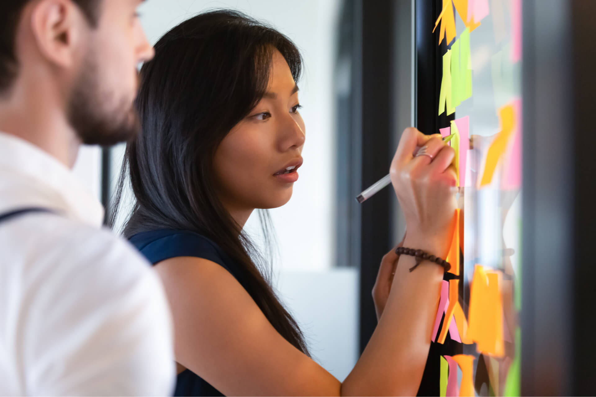 A woman writing on a sticky note with a colleague.
